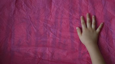 Bebekler buruşmuş kağıt mendil yüzeyine el sürerler. Eflatun kağıt ve çocuk avuç içinin üzerinde düz olmayan pembe kağıt dokusu.