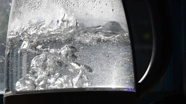 Blurry bubbles of boiling water in old transparent kettle at bright sunlight