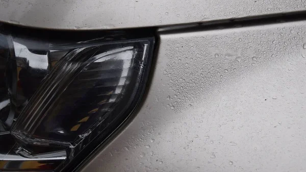 Texture of car bonnet with raindrops and headlight with blurry reflections — Stock Photo, Image