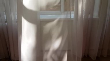 Şeffaf tül perdeler rüzgarda sallanıyor.