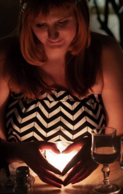 Kadın ellerini mum ışığında kalp şeklinde tutuyor.