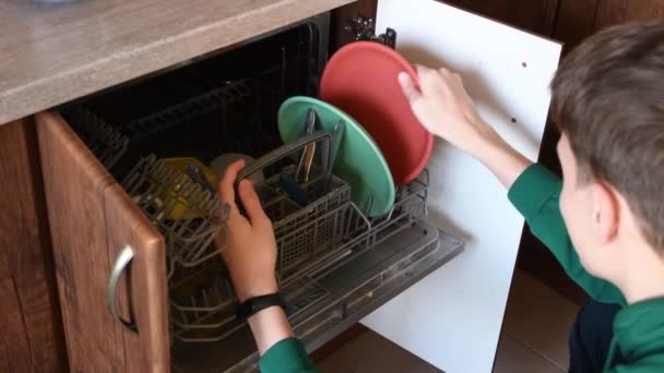 El joven toma platos limpios de la vajilla del lavavajillas. Hombre haciendo tareas — Vídeos de Stock