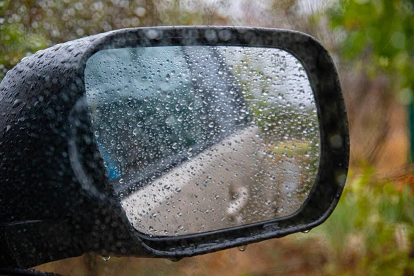 Shot through wet car window with side mirror in fall rainy weather