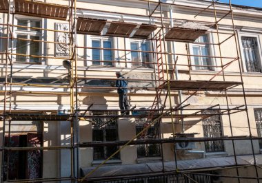 İnşaat işçisi tehlikeli iskelelerde güvenlik ekipmanı ve miğferi olmadan duruyor.