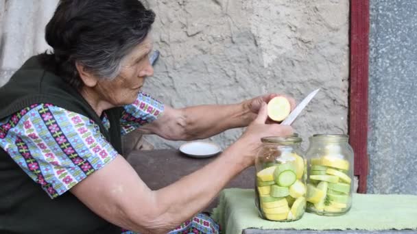 Mujer mayor de 80 años cortó calabacín fresco en rodajas y puso dentro de frascos de vidrio para enlatado casero — Vídeos de Stock