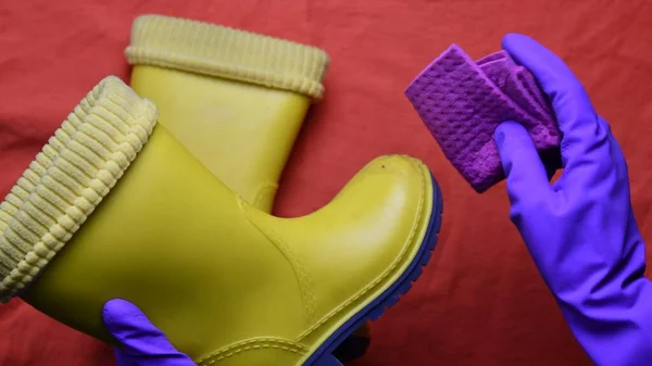 Hands in purple rubber gloves clean kids yellow rubber boots