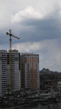 Gökyüzü arka planında vinç yelkeni olan bitmemiş çok katlı bir bina inşaatı. Çatı ve bulutlu inşaat halindeki şehir manzarası. Dikey çekim