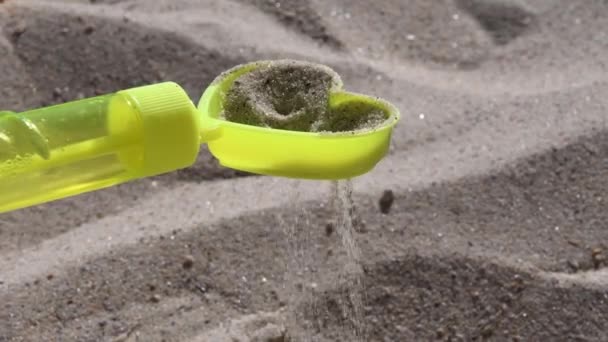 Mainan kuning pasir sifter dalam bentuk hati dengan menuangkan butir pasir di pantai — Stok Video