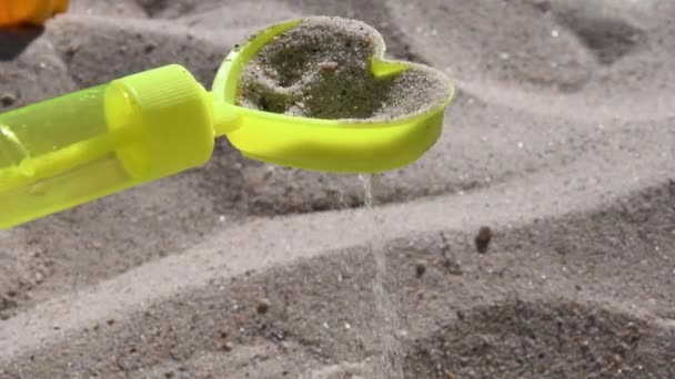 Żółty piasek zabawki przesiewacz w kształcie serca z wylewania ziaren piasku na plaży — Wideo stockowe