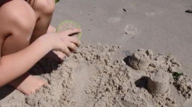 Çocuk kum kalıplı aletlerle kumdan kale yapıyor ve sonra da yalın ayak zıplayarak onu mahvediyor.