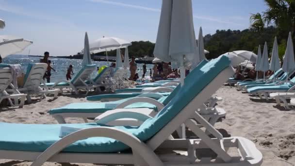 Leere Liegestühle auf weißem Sand am Strand und Sonnenanbeter — Stockvideo