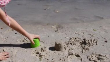 Çocuk kum kalıplı aletlerle kumdan kale yapıyor ve sonra çıplak ayakla onu mahvediyor.