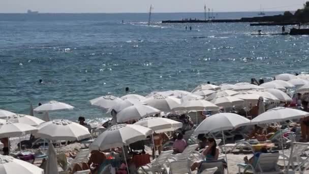 Летний морской пейзаж с белыми зонтиками на пляже с солярием и купанием людей — стоковое видео