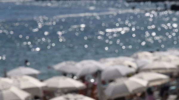 Defocused summer background with white parasols and blur beach seascape with sun flares over wavy water — Stock Photo, Image