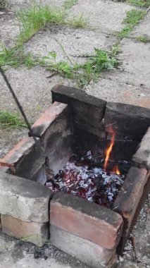 Kırsal alanda şöminenin içinde odun karıştırmak için ateş ütüsü kullanan adam duman ve küller havada uçuşuyor.