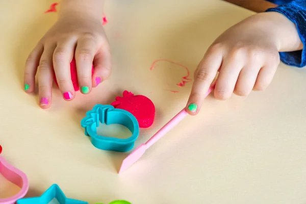 Child hands make strawberry shape from pink play dough using mold and toy forming tools for play clay