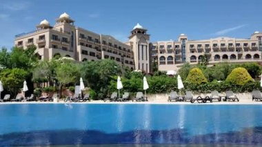 Boş güneşli yatakları ve havuz başında kapalı şemsiyeleri olan lüks bir tatil köyünde rüzgar havuz suyunu dalgalandırıyor.