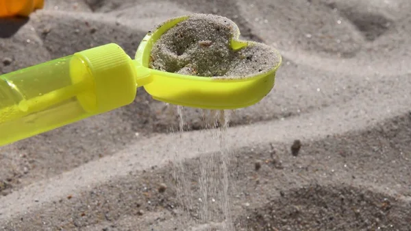 Peneira de areia de brinquedo amarelo em forma de coração com derramamento de grãos de areia na praia — Fotografia de Stock