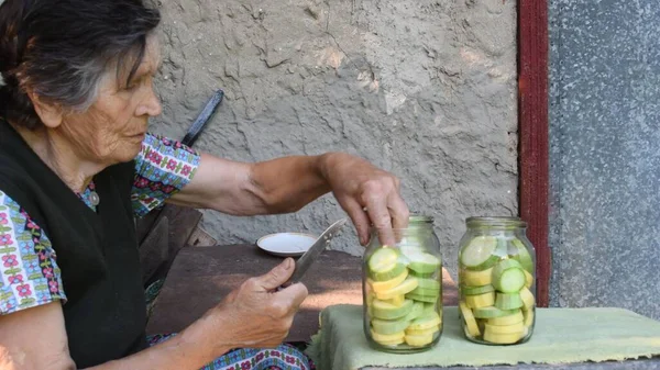 80s mulher sênior colocar fatias de abobrinha fresca dentro de frascos de vidro para enlatamento caseiro — Fotografia de Stock
