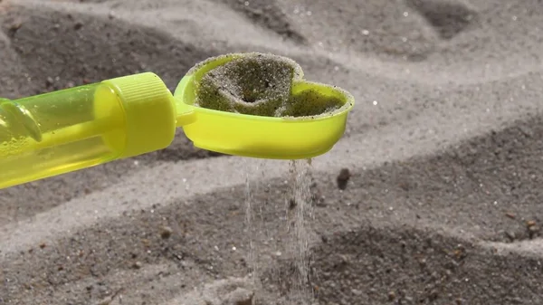 Peneira de areia de brinquedo amarelo em forma de coração com derramamento de grãos de areia na praia — Fotografia de Stock