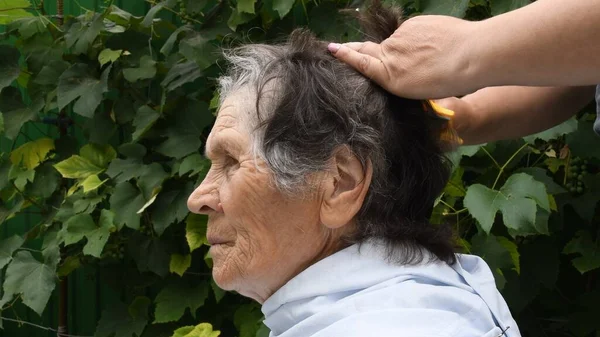 Mãos femininas cortando cabelo de mulher sênior no quintal — Fotografia de Stock