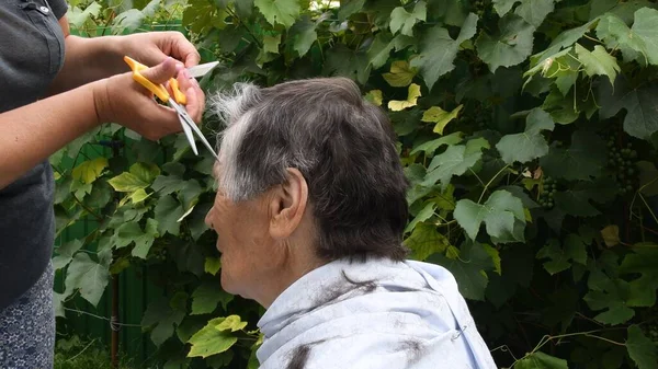 Руки стригут волосы на виске старушки с наполовину седой короткой стрижкой — стоковое фото