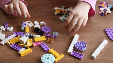 Küçük kız elleri küçük lego tuğlalarına ve oyuncaklarına dokunur ve çevirir.