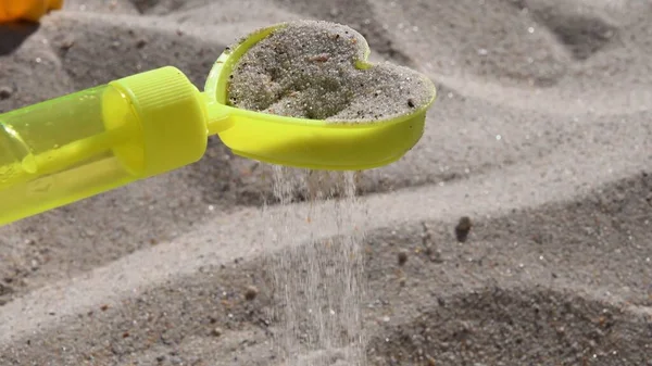 Peneira de areia de brinquedo amarelo em forma de coração com derramamento de grãos de areia na praia — Fotografia de Stock