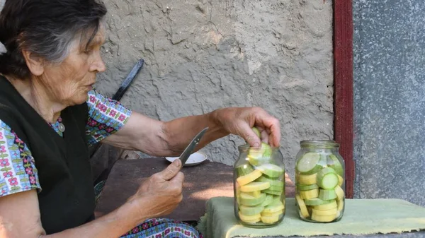 80s mulher sênior colocar fatias de abobrinha fresca dentro de frascos de vidro para enlatamento caseiro — Fotografia de Stock