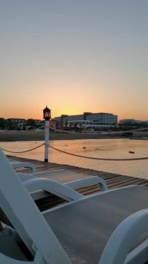 Boş güneşli yataklar ve klasik fener siluetiyle iskeleden gün doğumunun hızlandırılmış görüntüsü