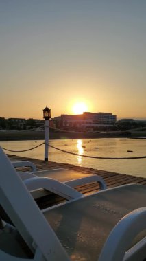 İskeleden yavaş çekim gündoğumu görüntüsü boş güneş yatakları ve klasik fener siluetiyle