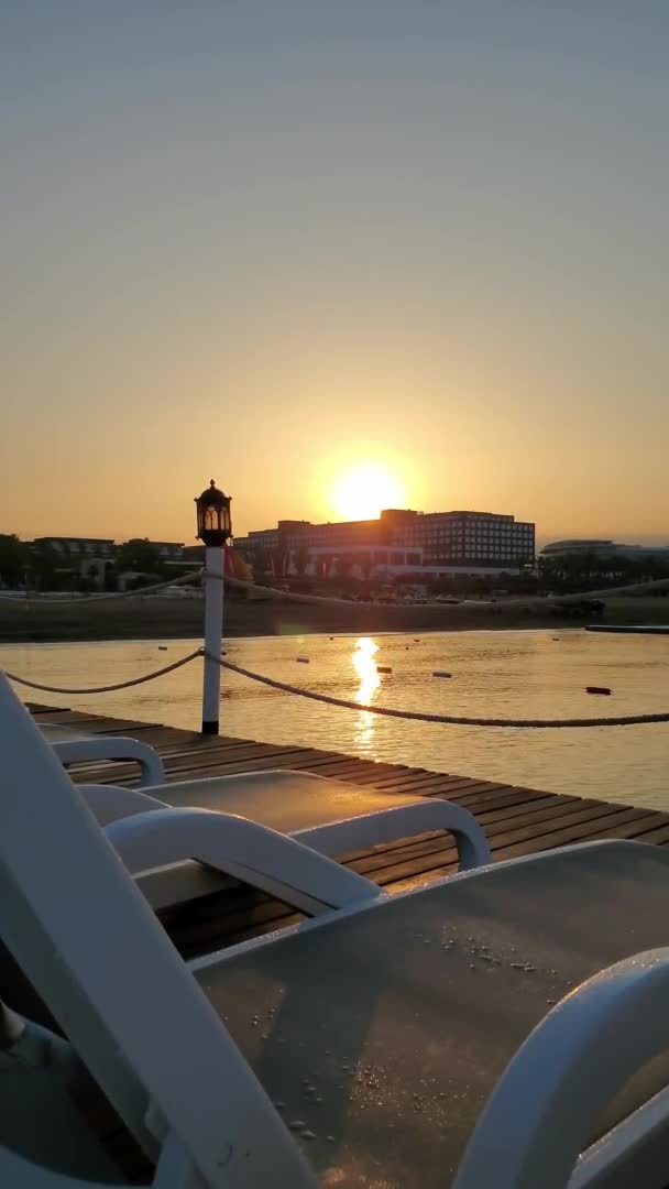 Vista del amanecer desde el muelle con tumbonas vacías y silueta de linterna vintage — Vídeos de Stock