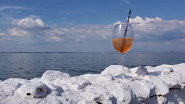 Statische Ansicht Cocktailweinglas auf weißem Steinzaun am Meer mit Meereswellen Hintergrund — Stockvideo