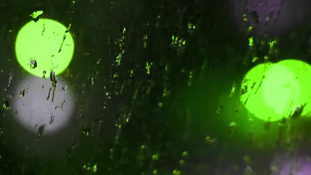 Des gouttes de pluie nocturne sur une fenêtre sale avec des lumières bokeh vert clignotant fond — Video