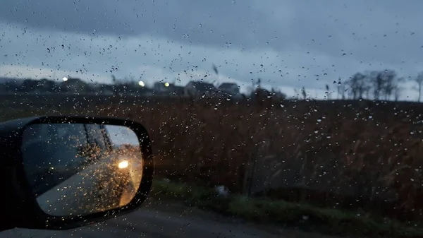 Shot through wet car window with side mirror in fall rainy weather — Stock Photo, Image