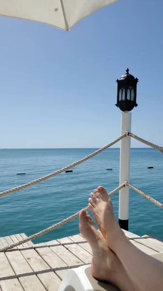 Pies descalzos en solárium en el muelle junto al mar con linterna vintage — Foto de Stock
