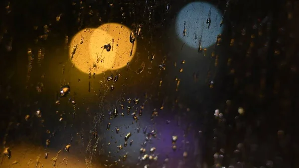 Drops of night rain on dirty window with bokeh lights background — Stock Photo, Image