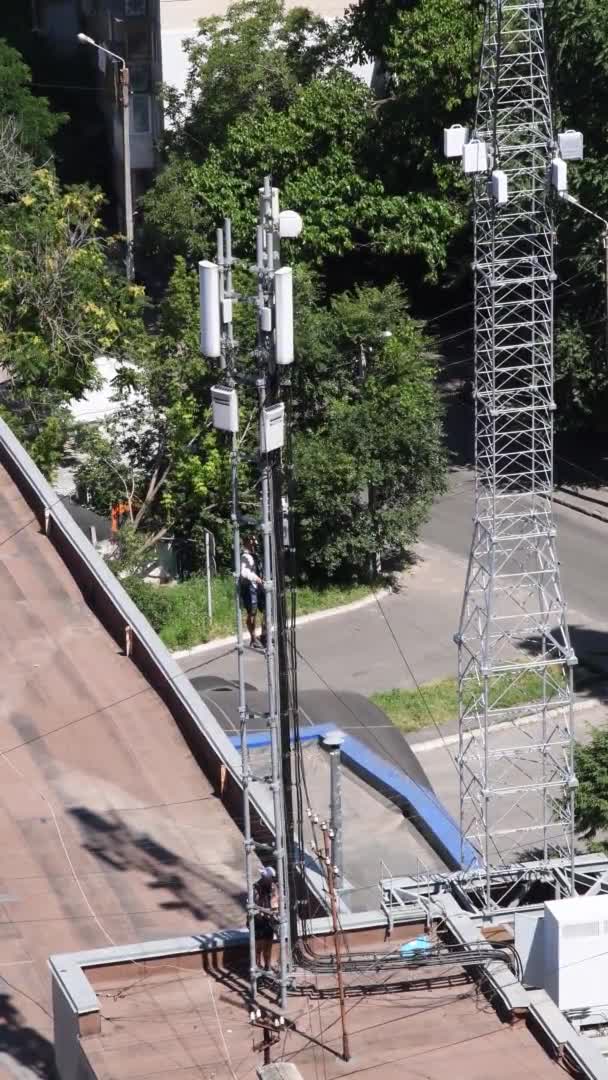 Неузнаваемые работники на крыше здания с коммуникационной башней — стоковое видео
