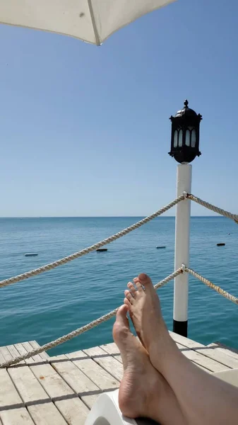 Pés descalços no solário no cais à beira-mar com lanterna vintage — Fotografia de Stock