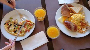 İnsanlar tabaktan çatal ve bıçakla yemek yer ve portakal suyu içerler.