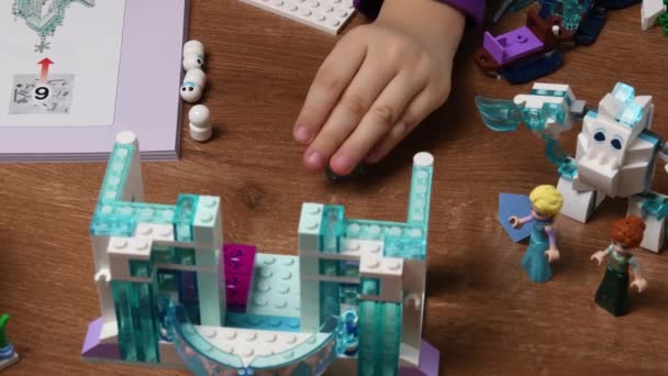 Batole ruka položí hračky Lego bloky na stůl a hraje s Frozen Disney hrad