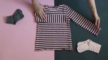 Female hands fold and stack child clothes on two colored grey pink background