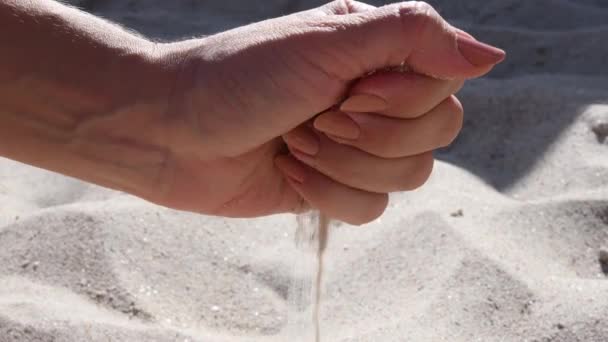 Os grãos de areia fluem por dedos da mão feminina na praia — Vídeo de Stock
