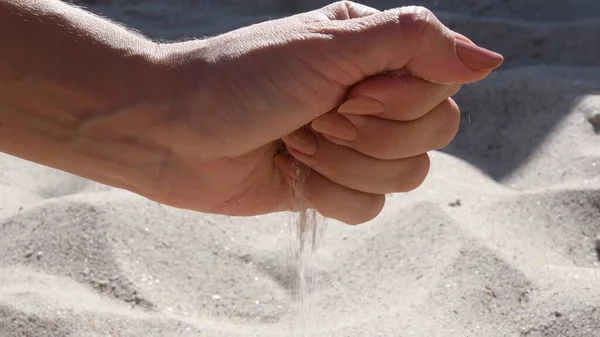 Sandkörner ergießen sich durch Finger weiblicher Hand am Strand — Stockfoto