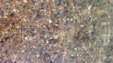 Çakıl taşı tabanlı arka planda POV ayakları saf deniz suyunda