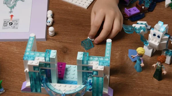 Mão de criança coloca tijolos de Lego de brinquedo na mesa e brinca com castelo Disney congelado — Fotografia de Stock