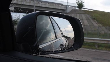 Yağmurlu havada hızla hareket eden arabanın yan aynasında bulanık bir görüntü.