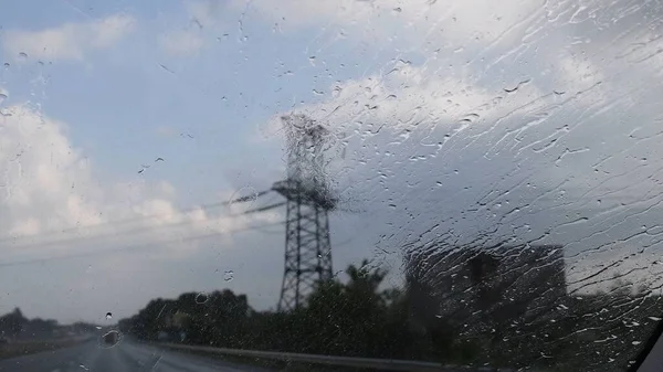 Autoscheibe mit spritzendem Regen und verschwommener Sendemast-Silhouette dahinter — Stockfoto