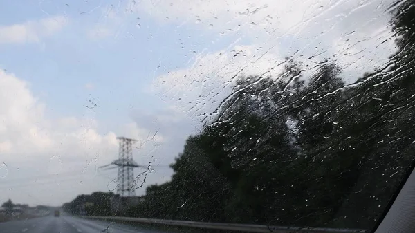 Parabrezza auto con spruzzi di pioggia e la silhouette della torre di trasmissione offuscata dietro — Foto Stock