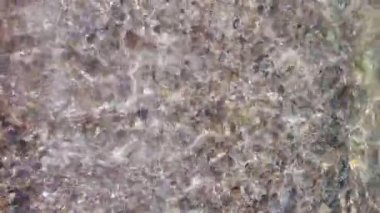 Çakıl taşının dibinde saydam deniz suyunda çıplak ayakla duran POV.